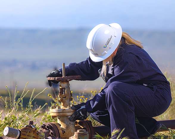 Employee wearing helmet turning valve with hills in the background